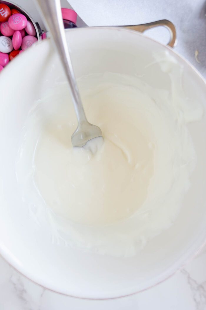 A bowl of white glaze being stirred with a metal spatula.