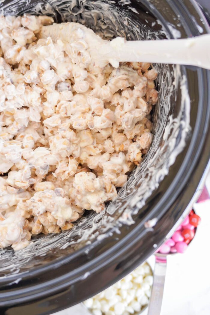 A close-up view of a creamy white chocolate and peanut mixture in a black pot with a white spatula.