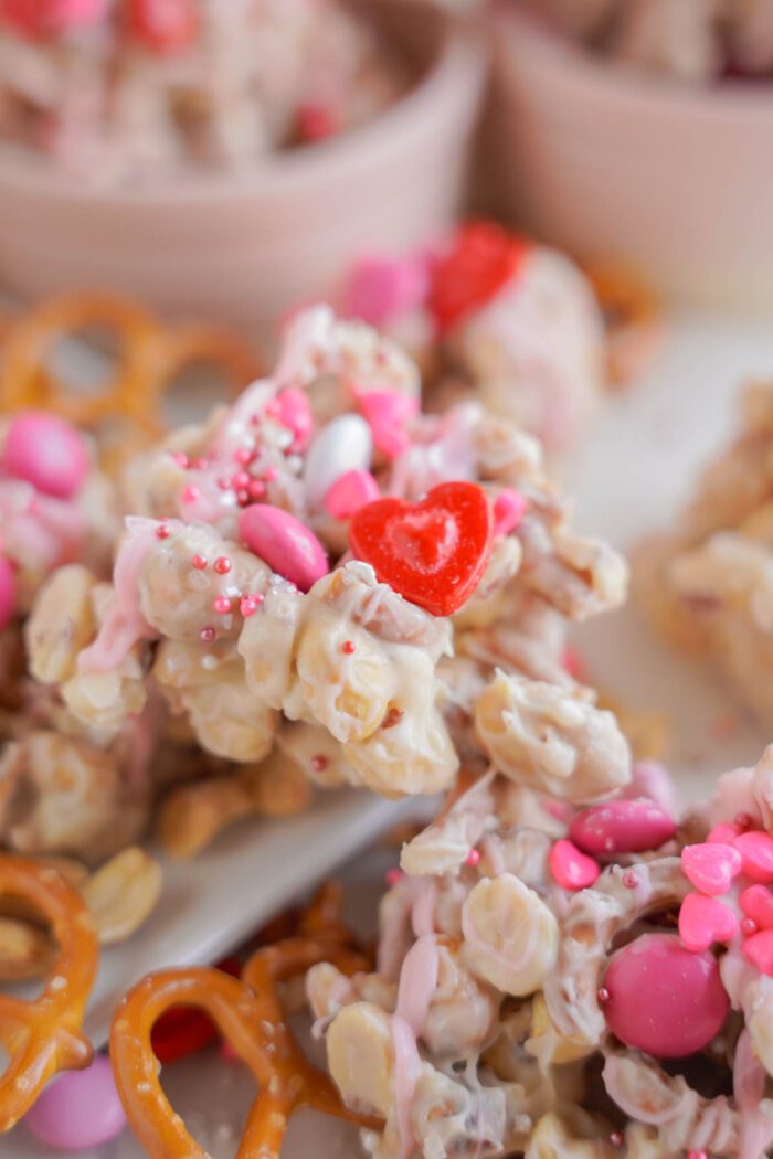 Close-up of white chocolate pretzel crockpot candy with pink sprinkles and a red heart candy on top.