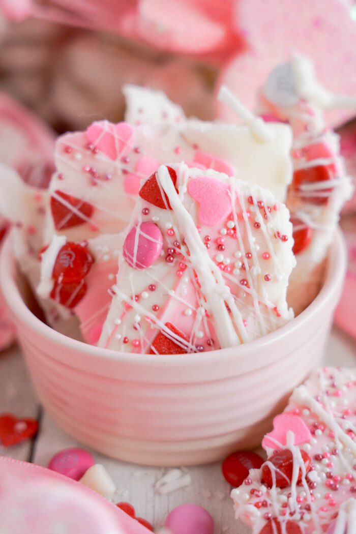 A bowl of White Chocolate Candy Bark garnished with red and pink sprinkles, presented on a festive background.