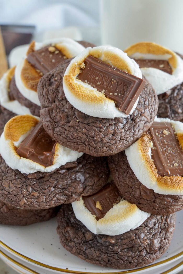 A stack of S'mores Cookies with melted marshmallows and Hershey's chocolate squares on top, served on a white plate.