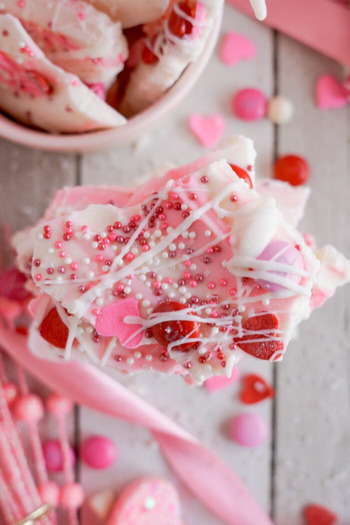 Valentine's Day Candy Bark decorated with sprinkles and small candies, displayed on a wooden surface with scattered candy hearts.