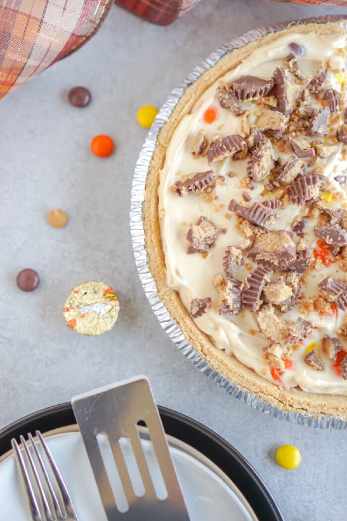 A top view of a reese's cheesecake, placed on a white plate with a pie server beside it, scattered candies around on a countertop.