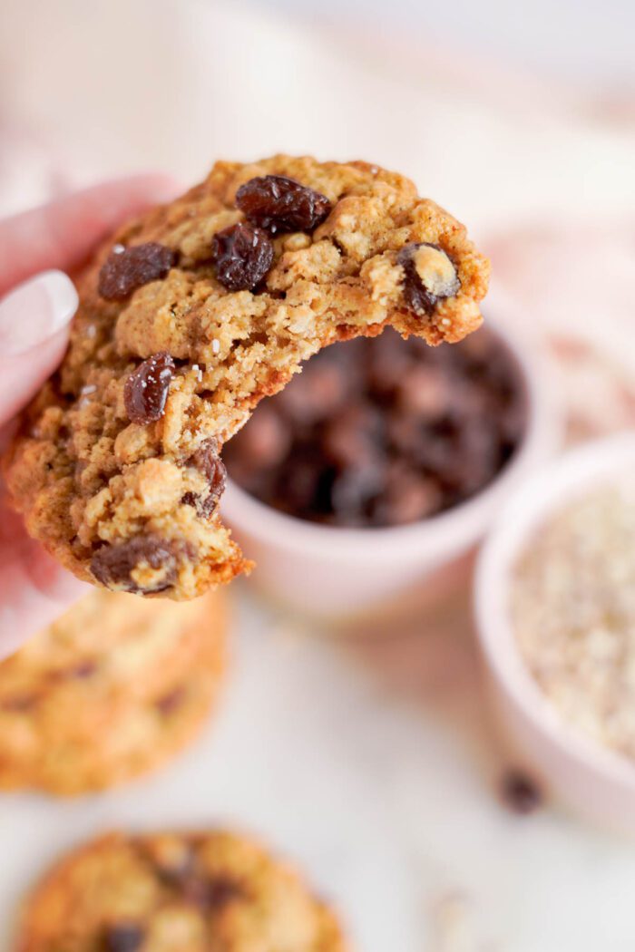 A close-up of a hand holding a freshly baked oatmeal raisin cookie from the best oatmeal raisin cookies recipe, broken in half to show its chewy texture.