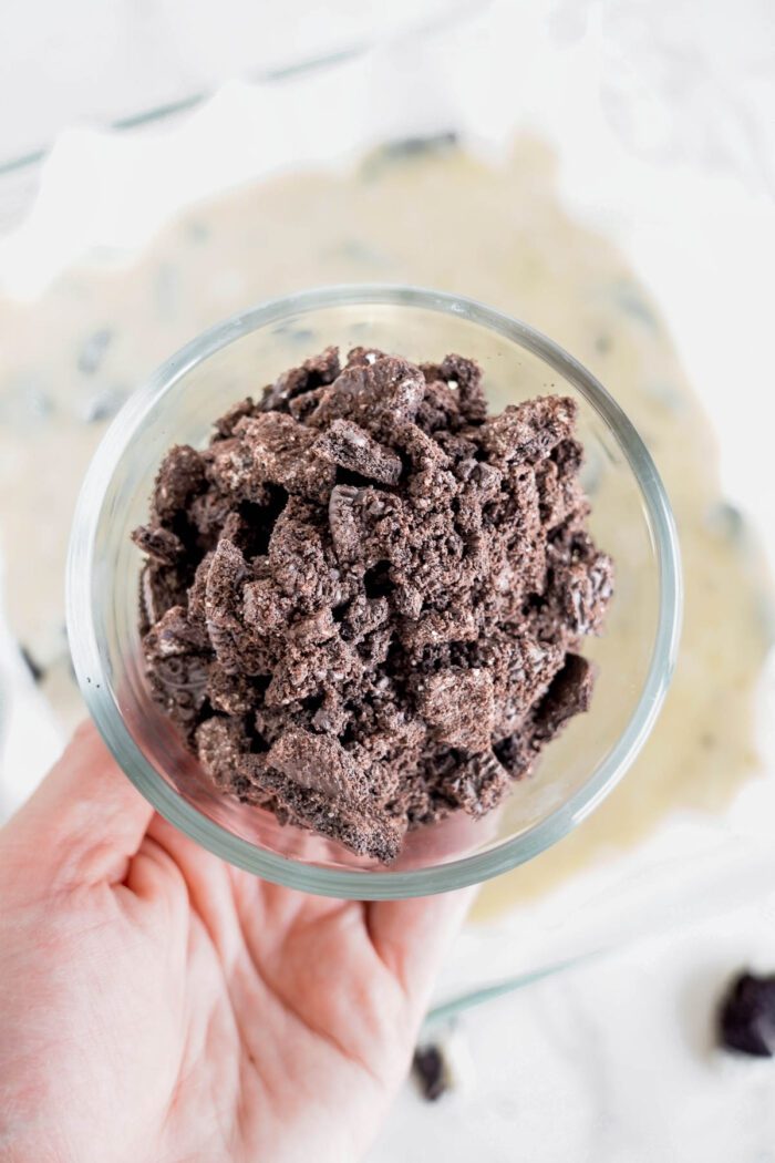 A person holding a bowl filled with chocolate cookie crumbs.