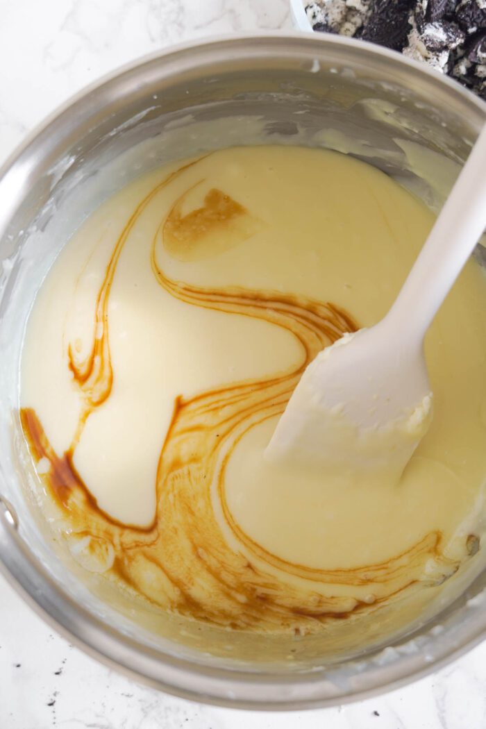 A bowl of fudge batter with vanilla being swirled in using a spatula.