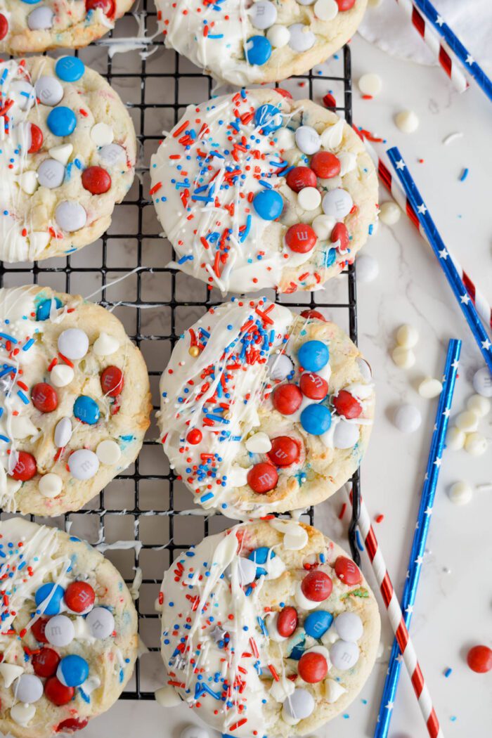 Easy 4th of July cake mix cookies with red, white, and blue m&ms and sprinkles on a wire cooling rack, surrounded by striped straws.