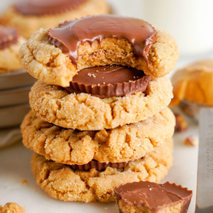 Peanut butter cookies with a chocolate piece in the middle, one cookie with a bite taken out, displaying its soft interior.