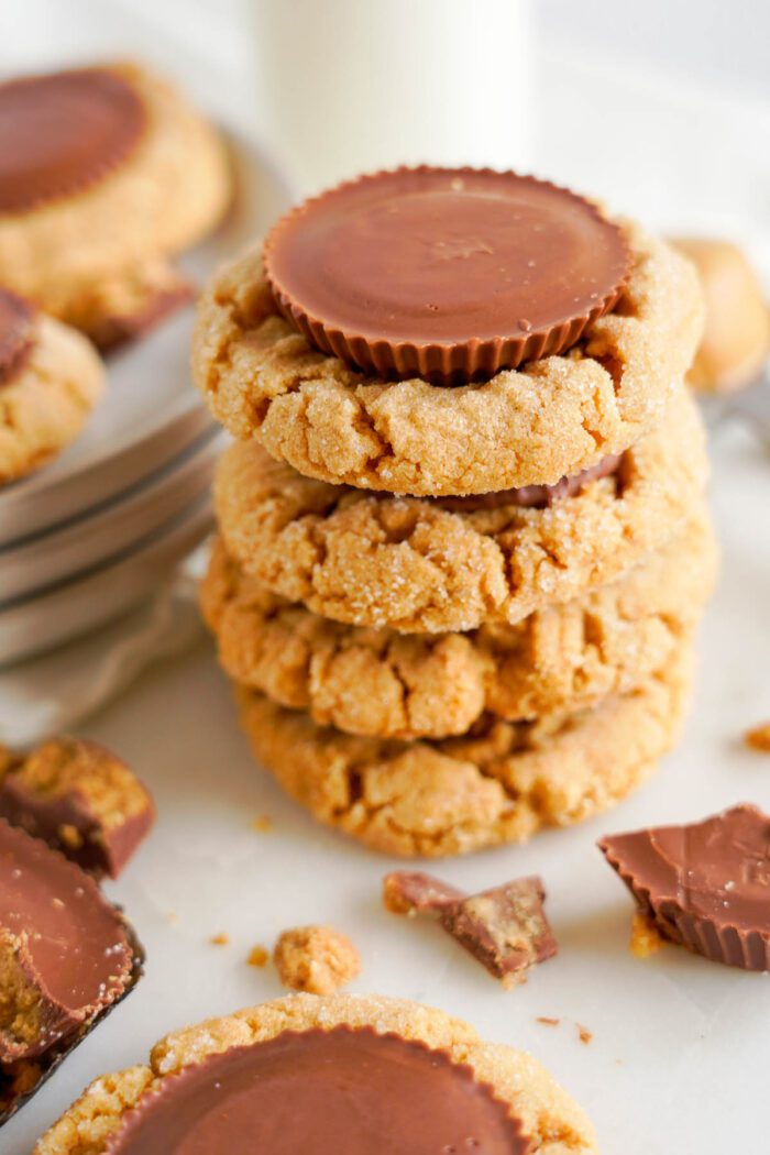 A stack of easy peanut butter cup cookies topped with a chocolate peanut butter cup, surrounded by cookie crumbs and pieces of chocolate.