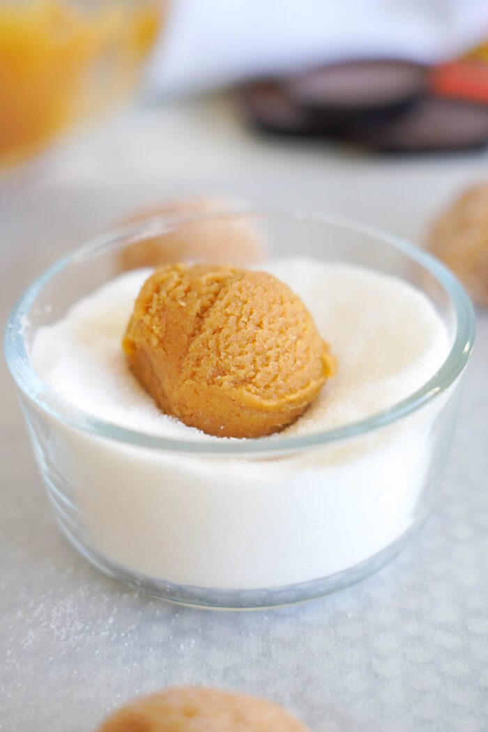 A scoop of pumpkin spice cookie dough placed on a layer of granulated sugar in a clear glass bowl, ready for an easy baking session.