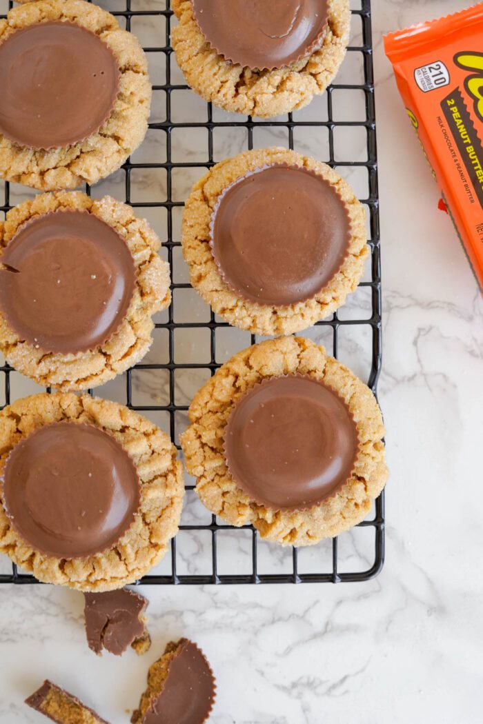 Easy homemade peanut butter cookies with chocolate disks, cooling on a wire rack beside a Reese's peanut butter cup wrapper.