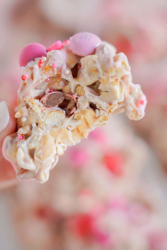 A close-up of a hand holding a piece of white chocolate crockpot candy with pink candy and sprinkles.