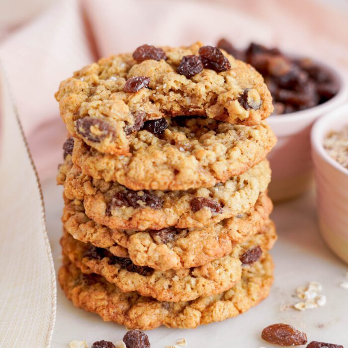 A stack of oatmeal raisin cookies with a bowl of raisins and oats in the background, showcasing the best oatmeal raisin cookies recipe.