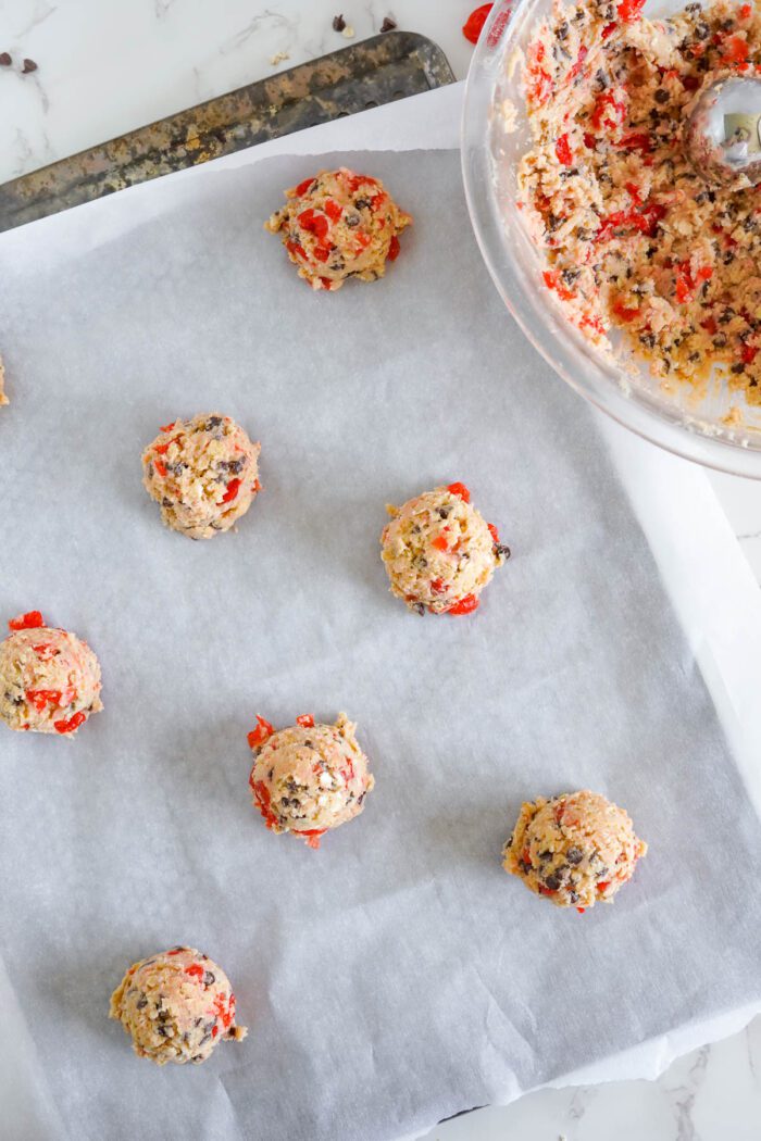 Cherry chocolate chip cookie dough scooped onto baking paper, ready to be baked.