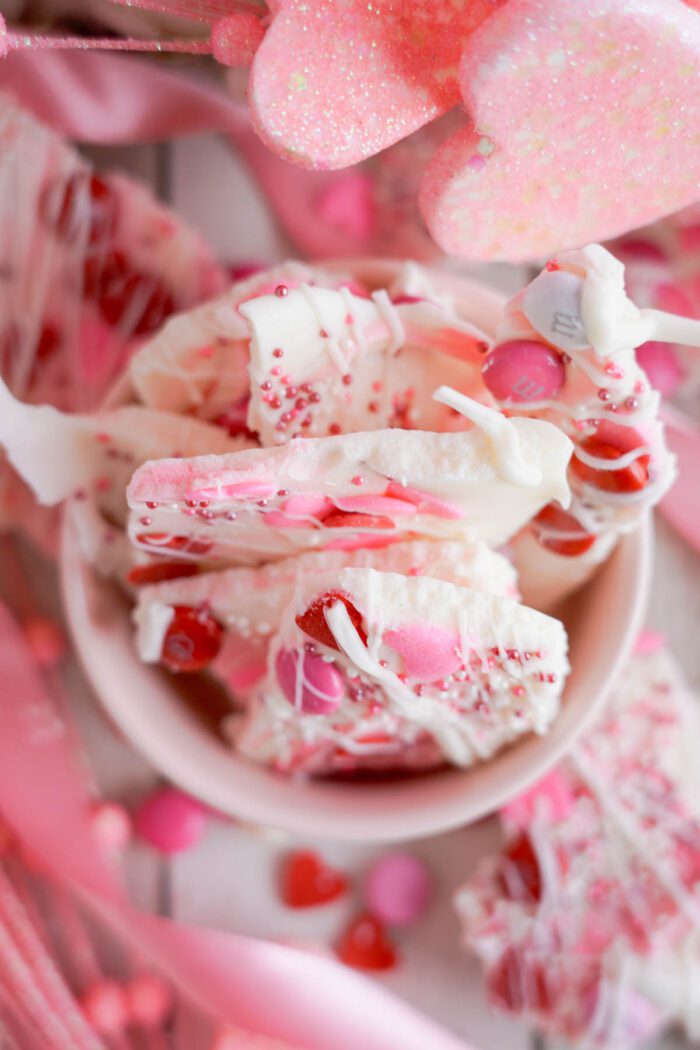 Valentine-themed bark candy with pink and white swirls, sprinkles and candy hearts, served in a pink bowl.