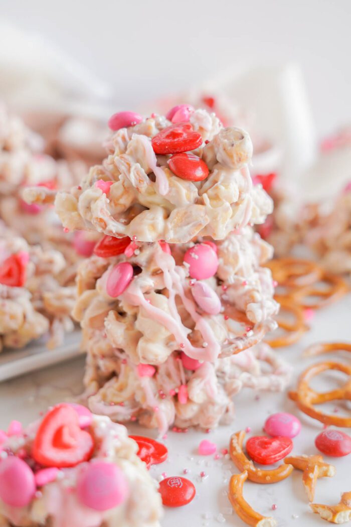 Stacks of white chocolate pretzel treats with pink drizzle and red candy toppings on a white plate.