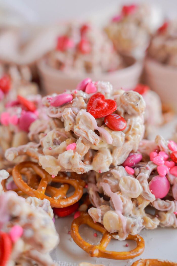 Close-up of a valentine’s day-themed snack mix with pretzels, cereal, and candies in pink and red colors.