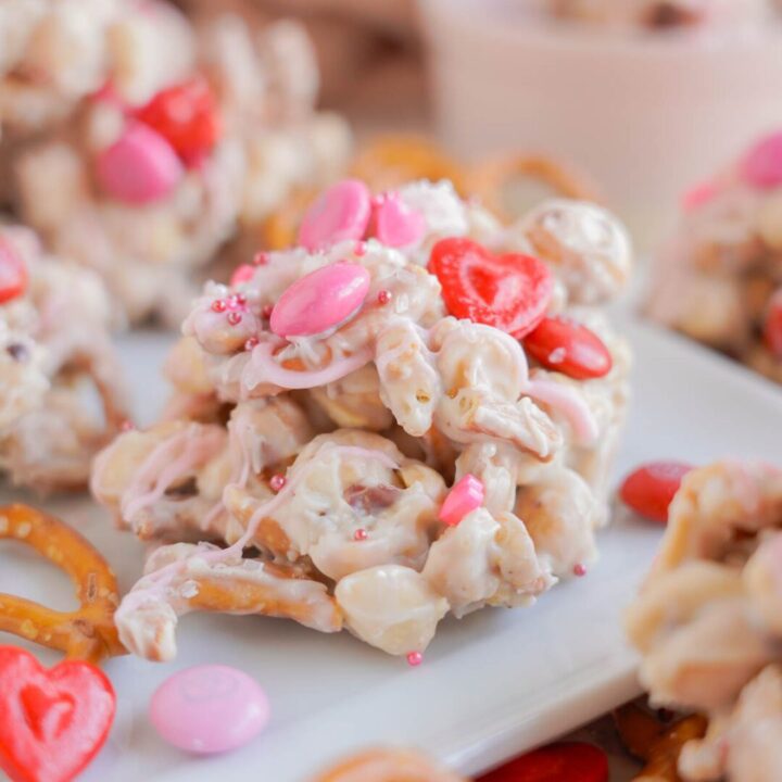 White chocolate pretzel candy with pink candies on a square white plate.