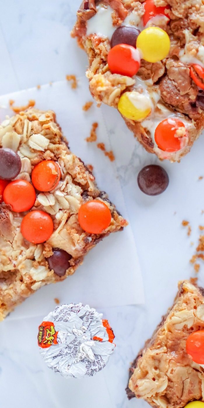 Homemade magic bar squares with peanuts, oats, and colorful candy pieces on a marble surface.
