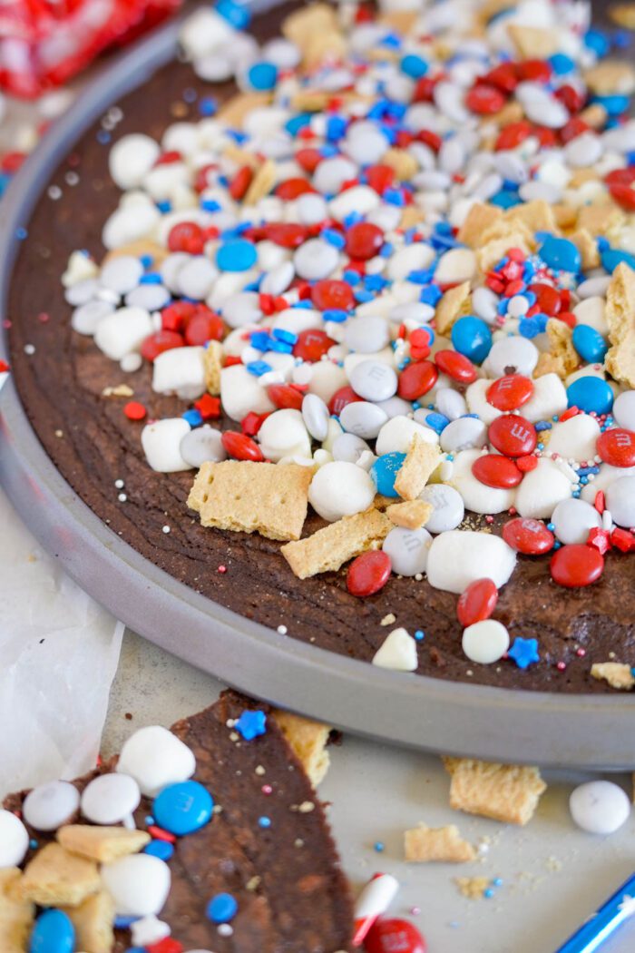 A close-up of a dessert pizza topped with red, white, and blue candies, marshmallows, and crumbled graham crackers.