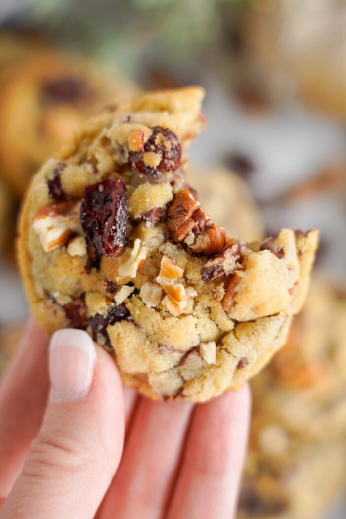 A hand holding a half-eaten cookie with nuts and chocolate chunks, showing detailed textures of the cookie's ingredients.