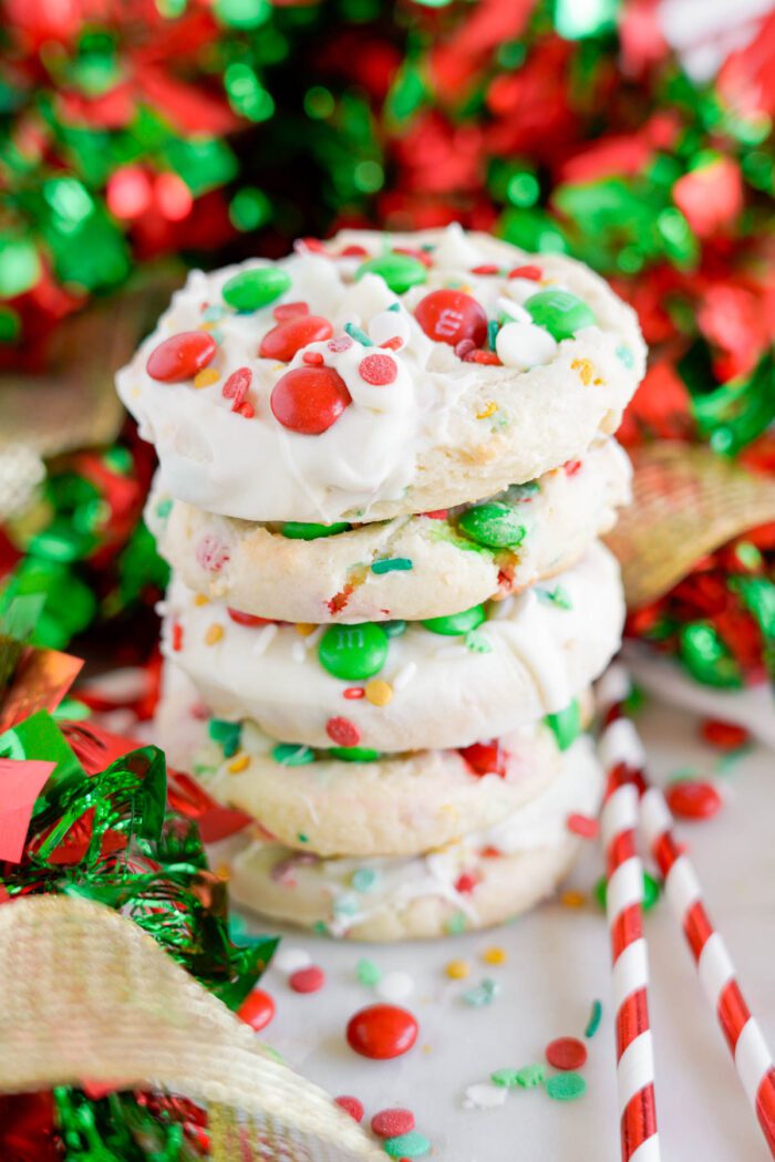 A stack of decorated holiday cookies with white chocolate and red, green, and white M&Ms surrounded by festive ribbons and straws.