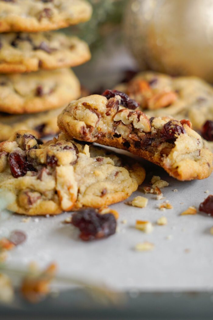 Close-up of cranberry and pecan cookies on a tray, with one cookie broken in half to show the chewy texture inside.