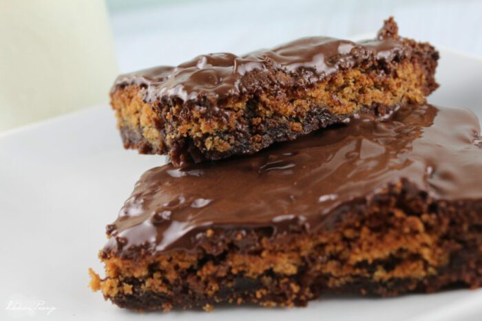 Two pieces of chocolate-covered, crumbly, brownie cookie bars on a white plate—a delightful example of peanut butter dessert recipes.