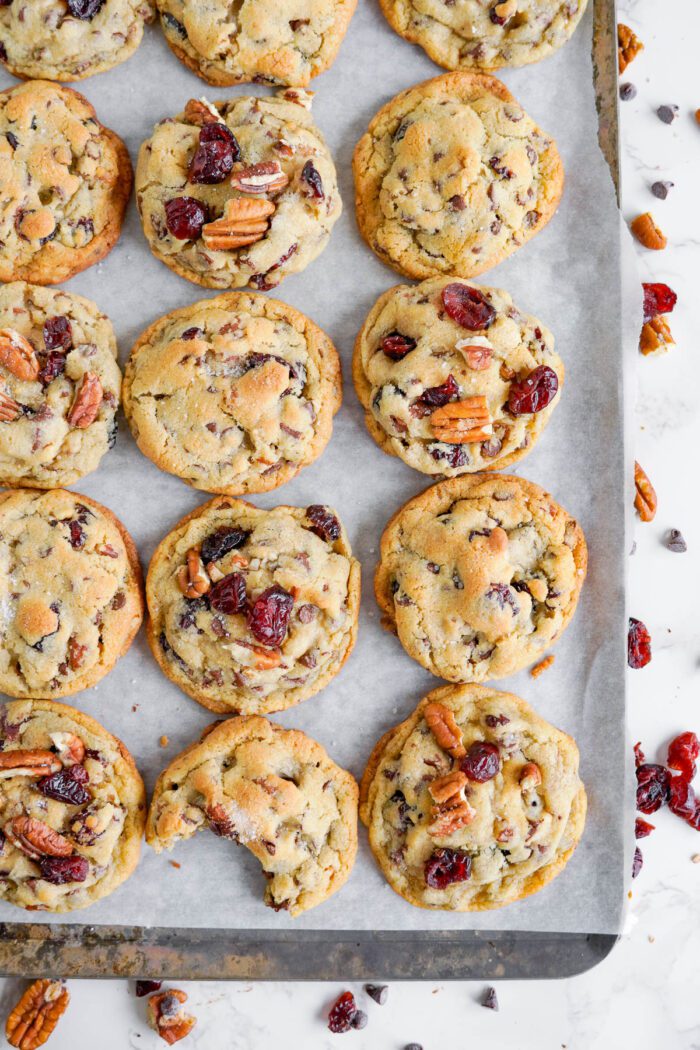 Freshly baked cookies with cranberries and pecans on a white surface.
