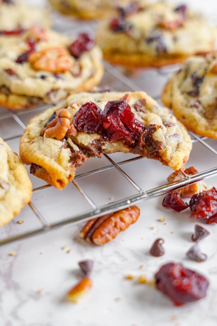 Homemade chocolate chip cookies with pecans and dried cranberries on a cooling rack.