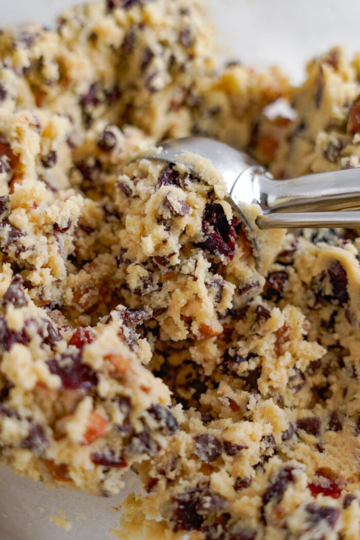 Close-up of cookie dough with cranberries and chocolate chips in a mixing bowl, with a spoon.