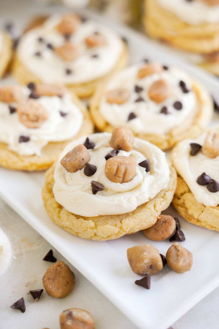 These easy cookie dough cookies are topped with creamy frosting and garnished with chocolate chips and small cookie dough pieces on a white plate.