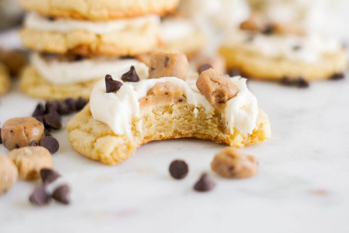 A partially eaten cookie with frosting, cookie dough pieces, and chocolate chips. Other cookies and scattered chocolate chips are visible in the background, creating a tempting scene straight from an easy cookie dough cookies recipe.