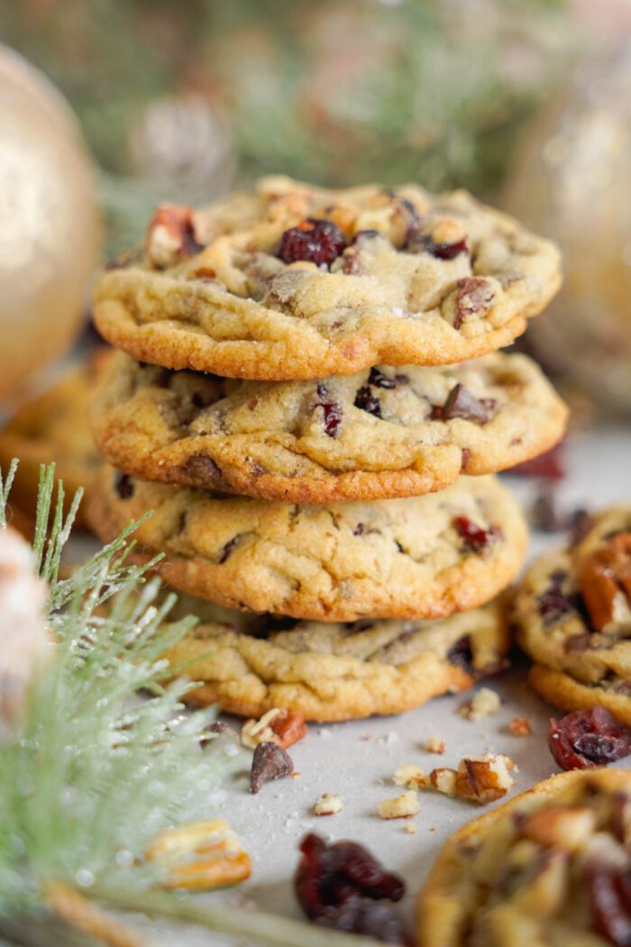 Stack of cranberry and pecan cookies on a festive table setting with blurred decorations in the background.