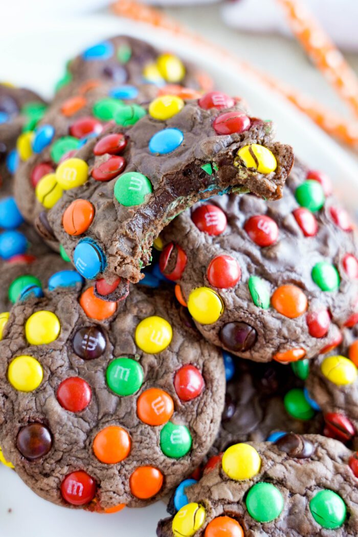 A stack of chocolate cookies covered in colorful candy-coated chocolates with a bite taken out of the top cookie.