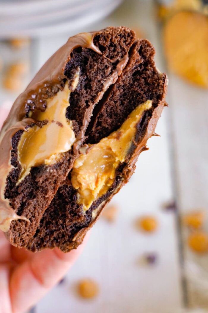 A close-up of a chocolate brownie cookie broken in half, revealing a peanut butter filling inside.