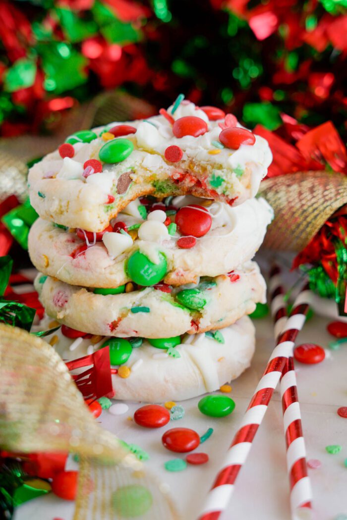 A stack of colorful Christmas cookies with red and green M&Ms and white chocolate, surrounded by festive decorations and candy canes.