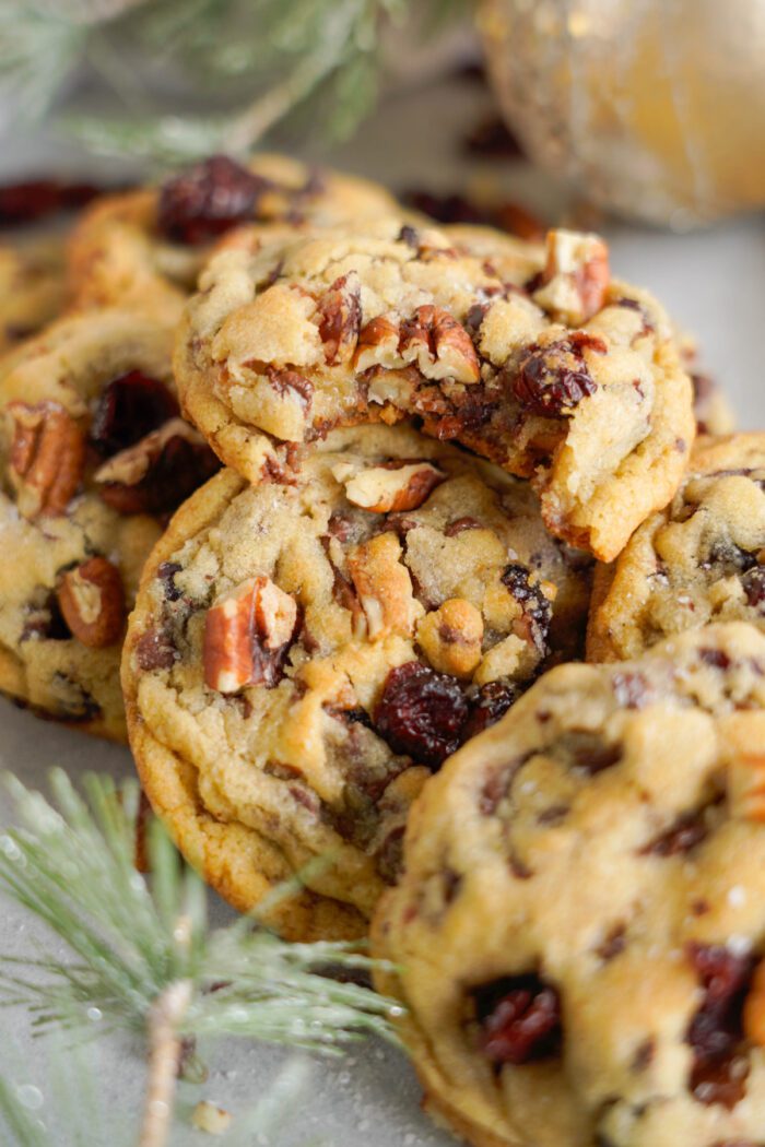 Homemade cookies with pecans and dried cranberries, displayed on a gray surface with a festive backdrop.