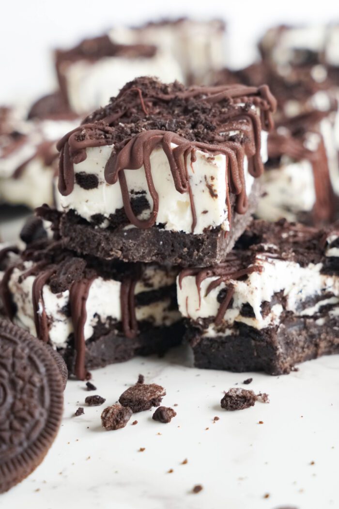 Oreo No Bake Cheesecake Bars drizzled with chocolate and stacked in a pile