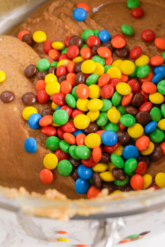 Colorful mini M&MS poured into a bowl of fudge batter.
