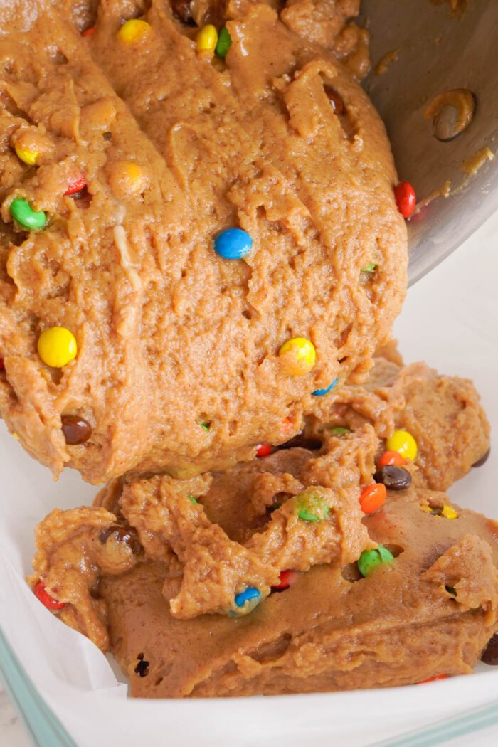 Cookie dough with colorful candy pieces being poured from a mixing bowl.