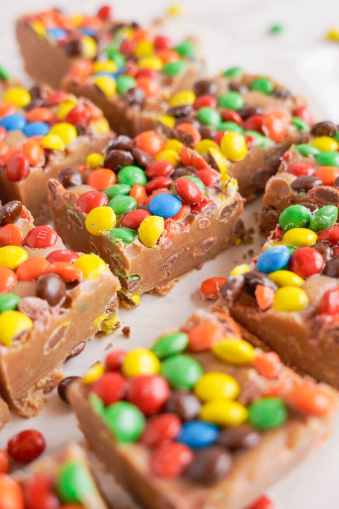 Slices of peanut butter fudge topped with colorful mini M&Ms on a white surface.