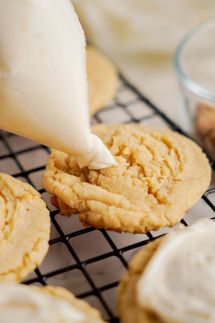 A piping bag is being used to frost peanut butter cookies on a cooling rack, bringing the Easy Cookie Dough Cookies Recipe to life.