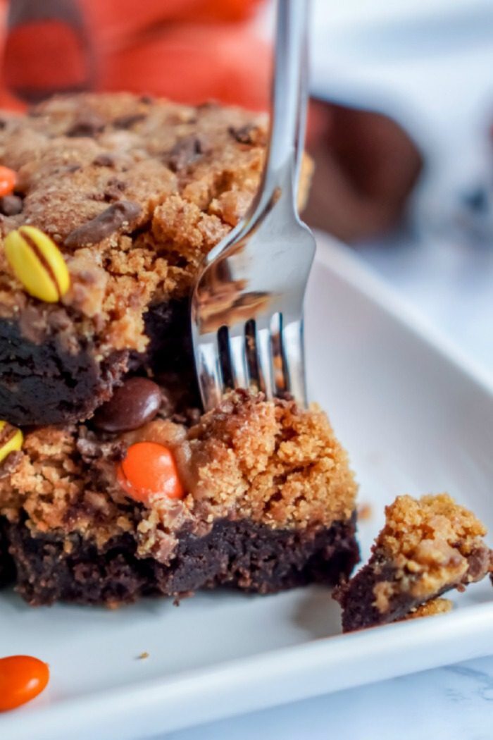 A fork is cutting into a layered dessert consisting of a brownie base topped with a crumbly cookie layer and decorated with colorful candies.