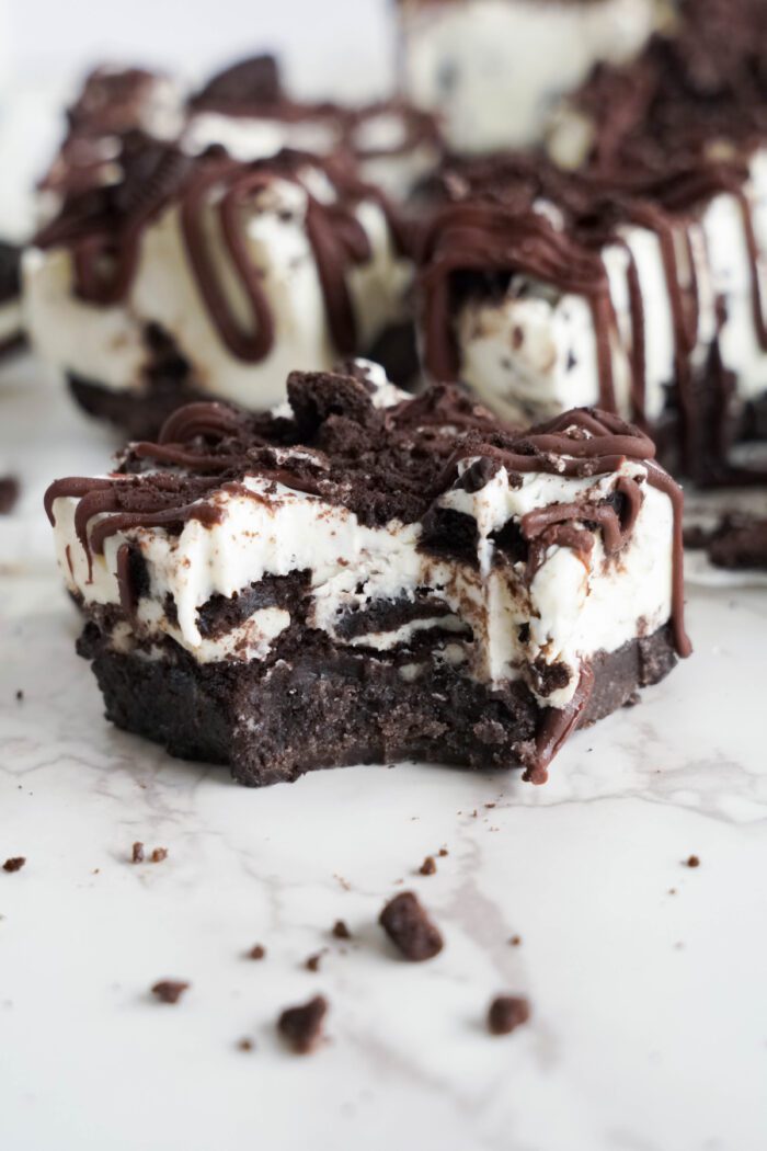 A close-up of a Oreo Cheesecake bar with cookie crumbles and chocolate drizzle, set on a marble surface.