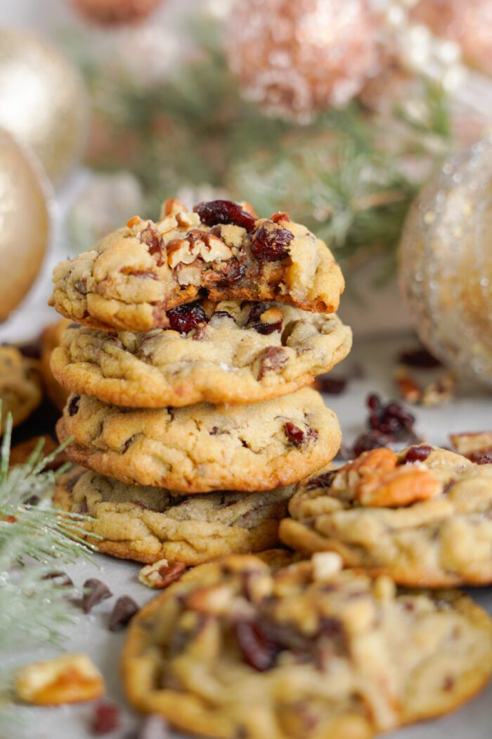 A stack of homemade cookies with nuts and dried cranberries, surrounded by festive christmas decorations.