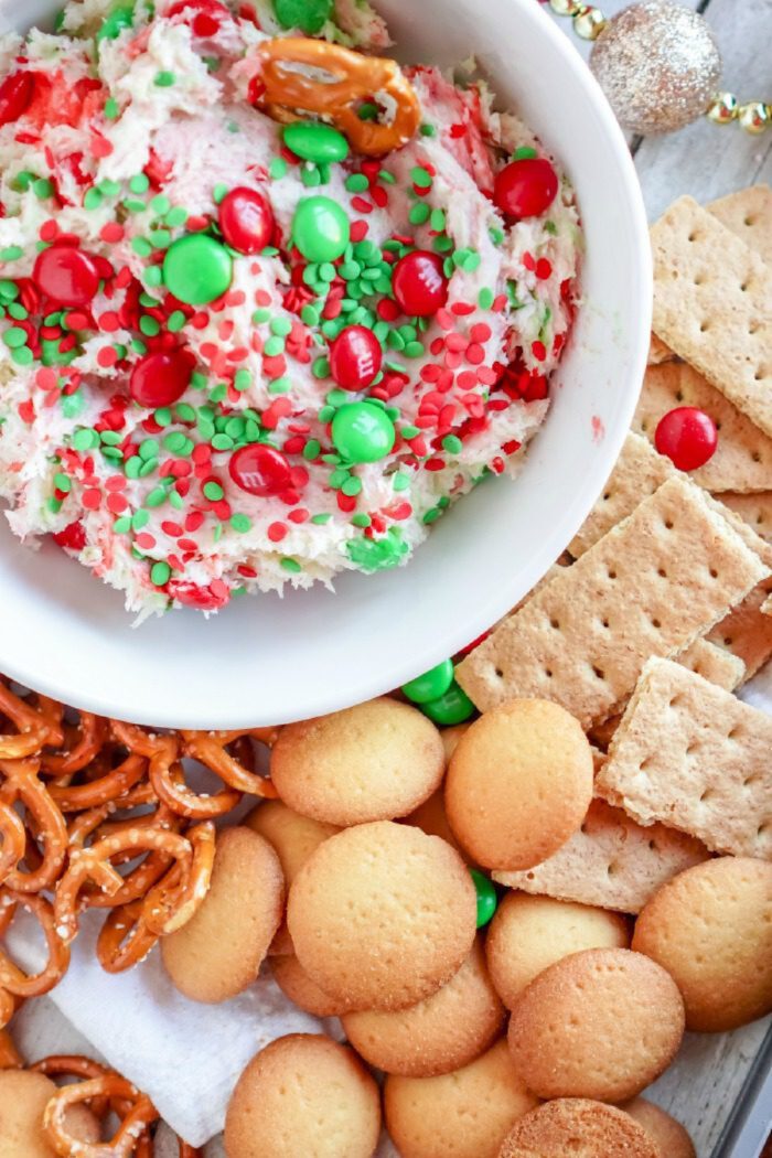 A bowl of festive dip topped with red and green candy and sprinkles, surrounded by pretzels, vanilla wafers, and graham crackers.