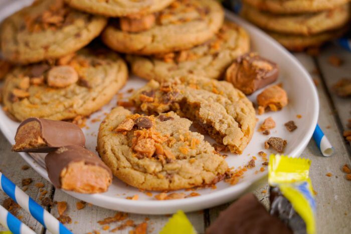 A plate of cookies with one cookie broken in half, surrounded by pieces of candy bars. Crumbs are scattered around the plate.