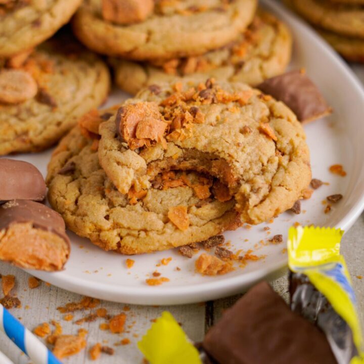 A plate of cookies with crumbled pieces and partially eaten cookie, surrounded by chocolate candies.