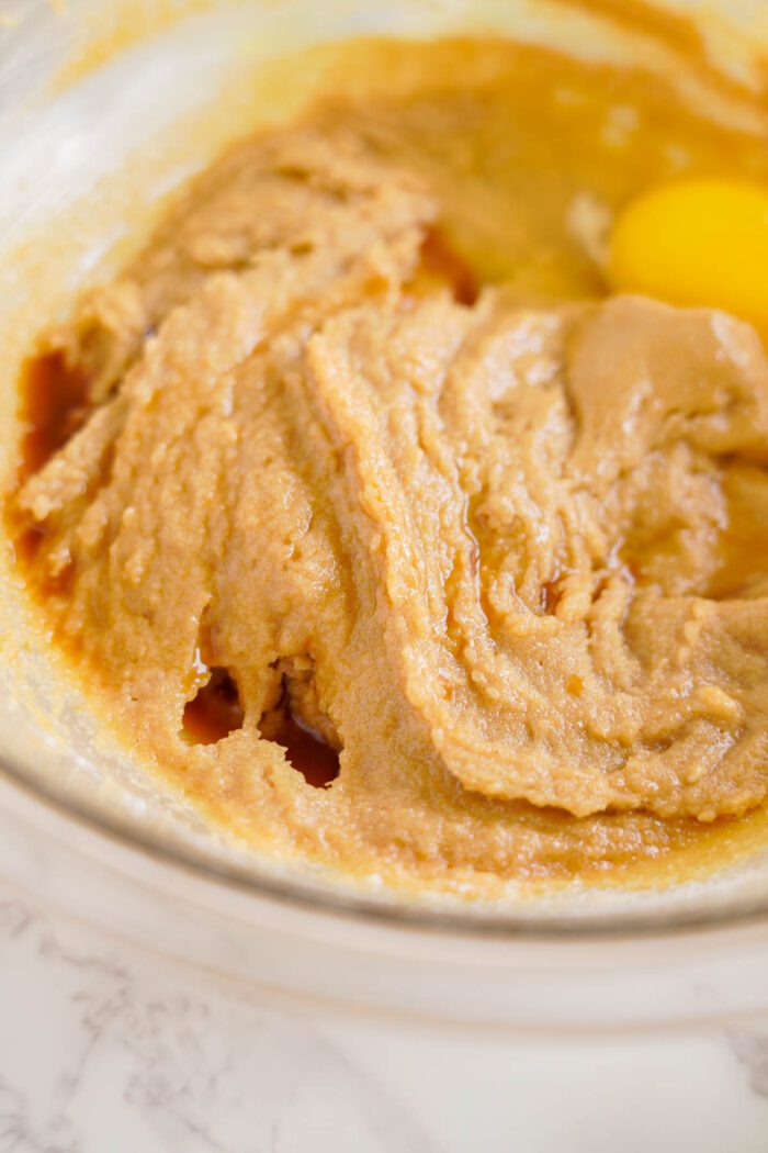 Close-up of a bowl containing partially mixed dough and an unmixed egg. The dough appears to be in the early stages of preparation.